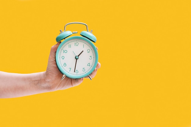 Alarm clock in a female hand on yellow