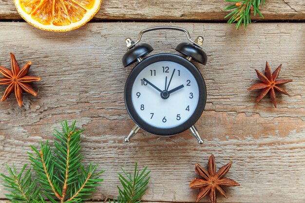 Alarm clock fir branch pine cones orange slices on old wooden background