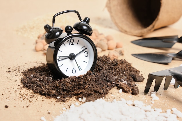 Alarm clock, gardening items, soil additives and fertilizers on kraft paper, copy place, gardening concept, time to plant seeds