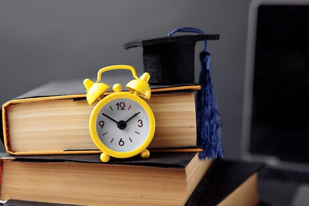 Alarm clock, graduation cap and books on table.