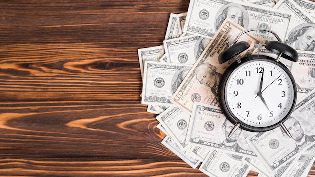 Photo alarm clock over the hundred dollar currency notes on wooden textured background