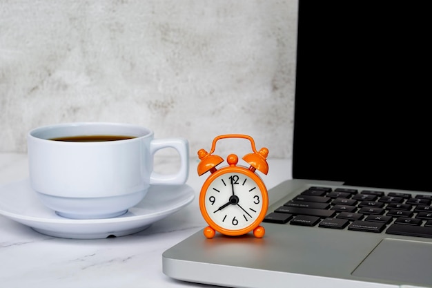 Alarm clock on laptop or notebook with coffee cup on a table The clock set at 8 o'clock Business concept