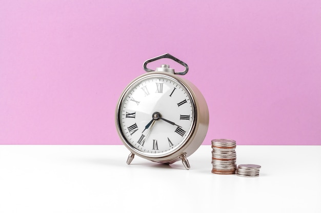 Alarm clock and money coins on the table.