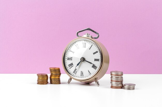 Alarm clock and money coins on the table.