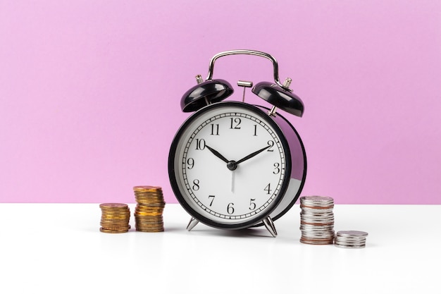 Alarm clock and money coins on the table.