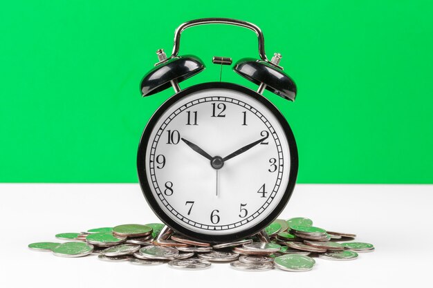 テーブルの上の目覚まし時計とお金のコイン。
