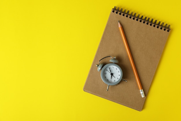 Alarm clock, notebook and pencil on yellow