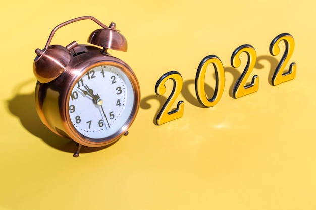 Alarm clock and numbers 2022 with hard shadow on yellow background. New year celebration minimal concept. Close up with copy space