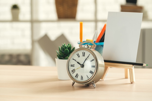 Alarm clock and office stationery objects close up on wooden table