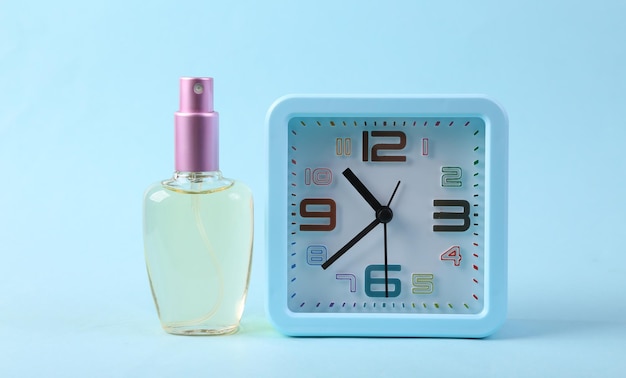 Alarm clock and perfume bottle on blue background