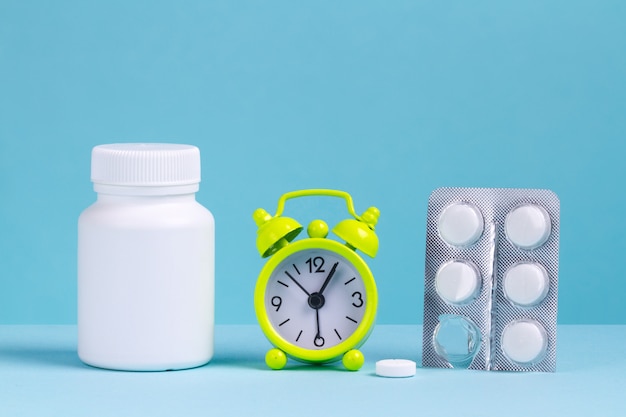 Alarm clock, pills, a jar of medicine on a blue background.