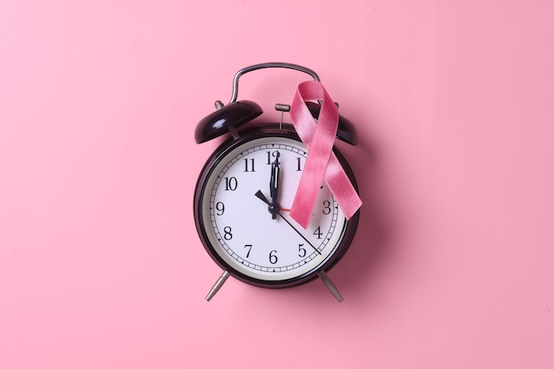 ピンクの背景に目覚まし時計とピンクのリボン。 10 月の乳がん啓発月間、世界のがん。