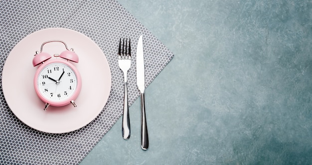 Photo alarm clock and plate with cutlery. concept of intermittent fasting, lunchtime, diet and weight loss