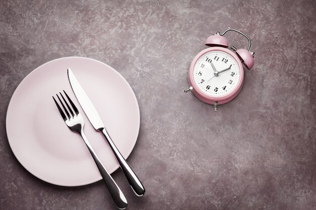 Alarm clock and plate with cutlery. 