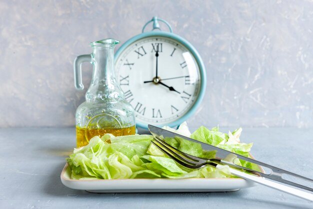 Alarm clock and plate with green iceberg lettuce and olive oil