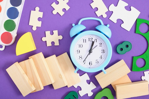 Alarm clock, puzzles, dominoes, paints, glasses, educational\
toys on a purple background top view, back to school concept, early\
childhood development