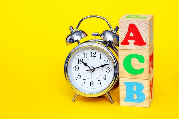 Alarm clock and red A, green C and blue B on wooden cube box isolated on yellow background