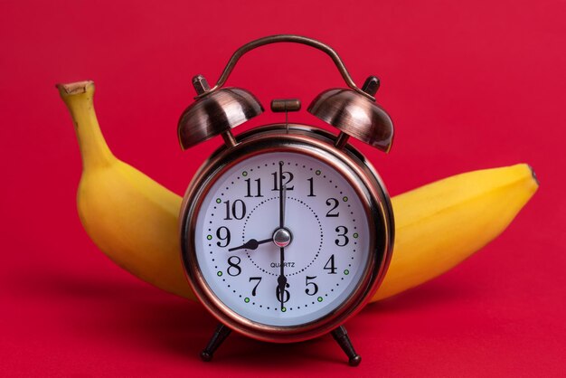 Photo alarm clock and ripe banana on a red background, the concept of a healthy dinner