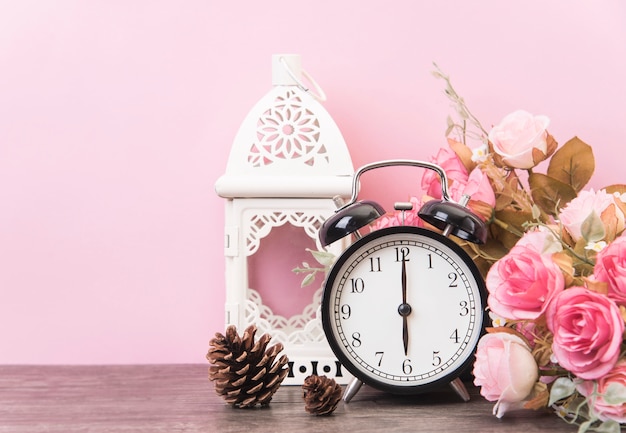 目覚まし時計、ピンクの背景を持つ木製テーブルにバラ