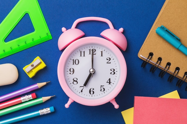 Alarm clock and school supplies on a blue surface