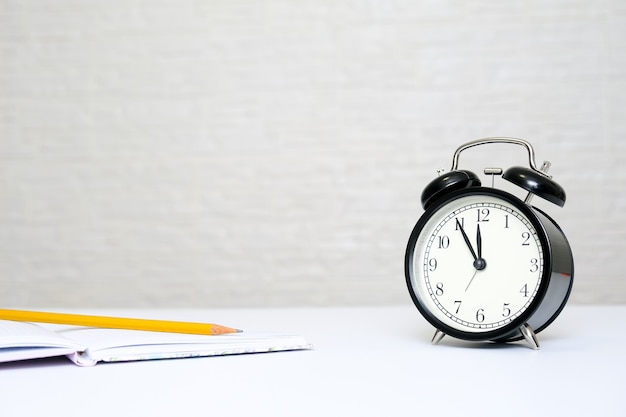 Photo alarm clock showing 5 minutes to twelve and a notebook with a yellow pencil as a concept of business tax report deadline with copy space.