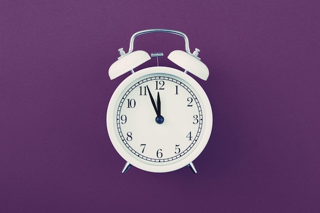 Alarm clock showing five minutes to twelve on a purple background.