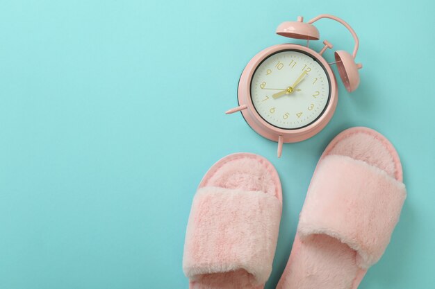 Alarm clock and slippers on blue background