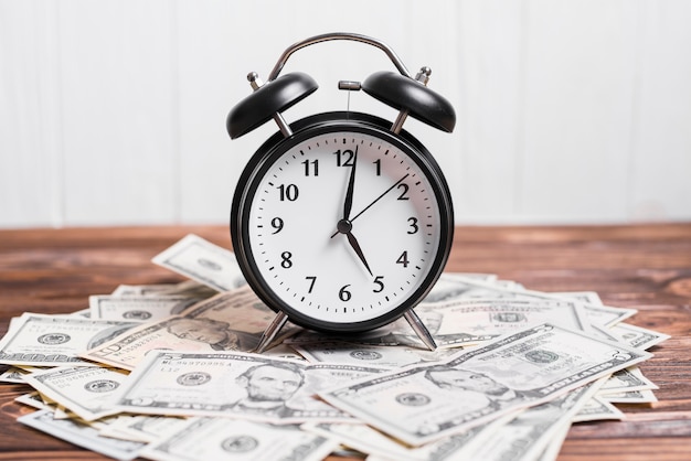 Photo alarm clock on spread currency notes over wooden textured background