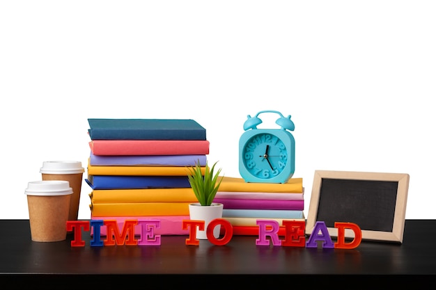 Alarm clock stack of books and cup on tabletop against white background