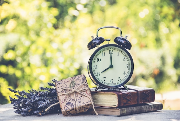 Alarm clock on stack of books on green background.