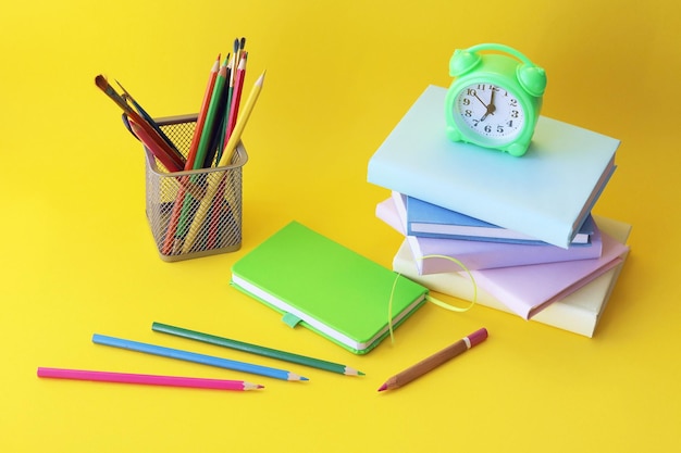 Alarm clock stack of books and stationery on yellow background back to school holidays