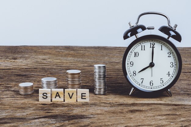 Alarm clock and stack of coins with Words SAVE made block wooden letters