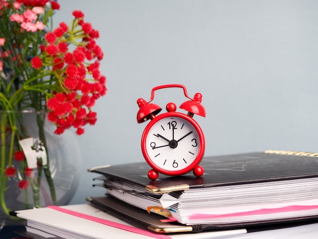 Alarm clock standing on table by stack of books against plain background