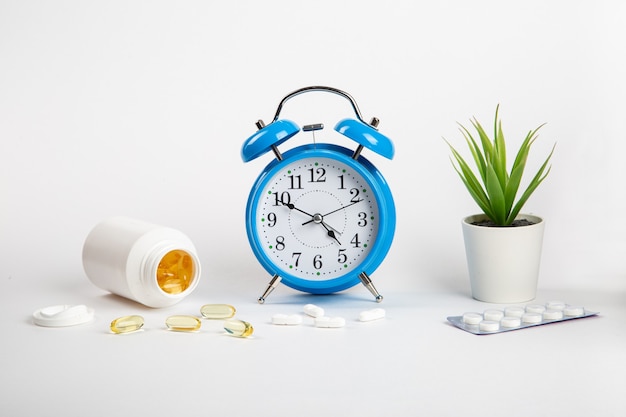 The alarm clock stands on a white wall shows the time of taking medications and next to it medical pills.