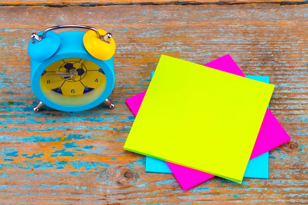 Alarm clock and a  sticky notes with empty space for a text on wooden background.