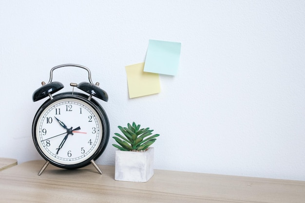 Alarm clock and succulent on wooden table with blank sticky notes on the wall