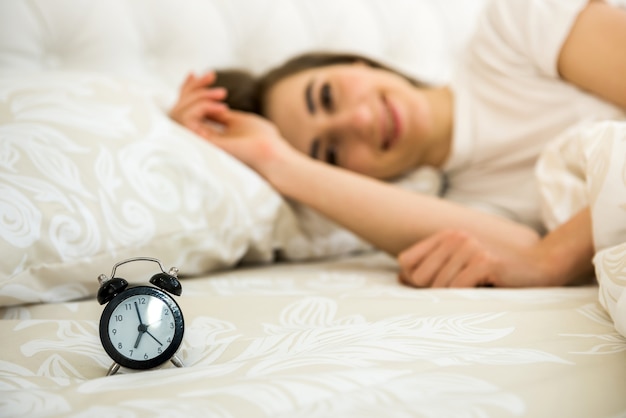 Alarm clock on table and woman sleeping in wall.