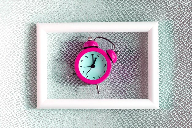 Alarm clock and white photo frame on color background Minimal concept