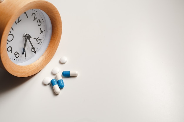 Alarm clock and white pills on white table 