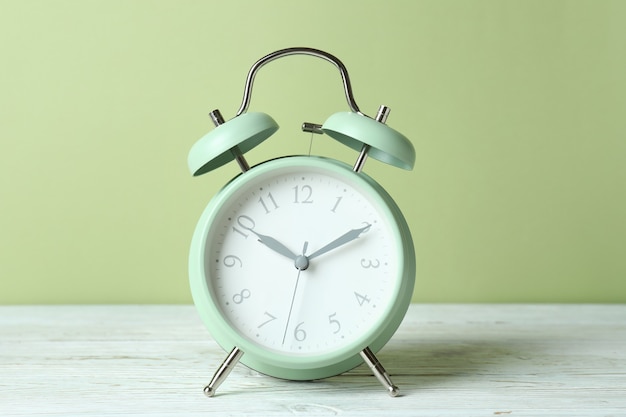 Alarm clock on white wooden table against green