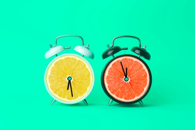 Alarm clock with citrus fruit concept Lemon or orange and clock on empty color background Vitamins