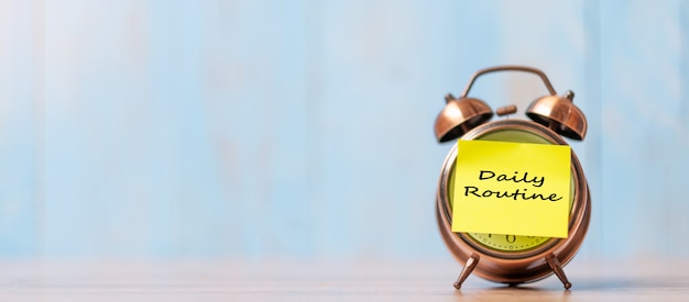 Alarm clock with Daily Routine note paper on wooden table