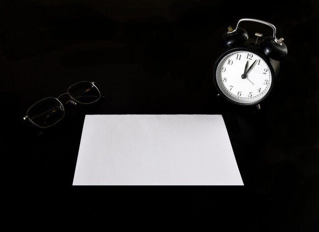 Alarm clock with empty blank sheet of paper on a black table next to the glasses