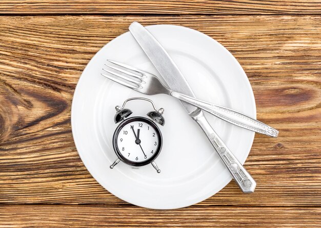 Foto sveglia con coltello a forchetta e piatto sul tavolo vista dall'alto tempo per mangiare