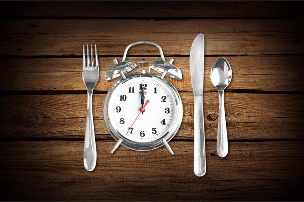 Alarm clock with knife, spoon and fork  on wooden background