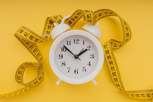 Alarm clock with measuring tape on a yellow background Diet concept