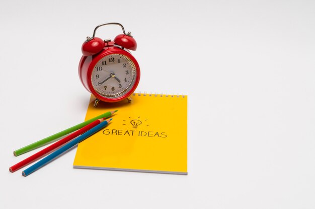 Alarm clock with notepad and colored pencils on white background Back to school Great ideas