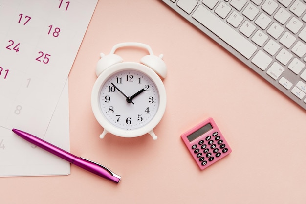 Alarm clock with sheets of calendar pen and keyboard on a pink background time management concept