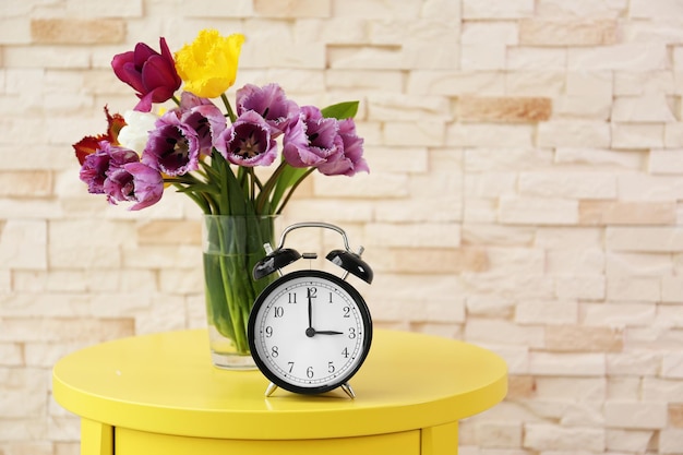 Alarm clock with tulips bouquet on table