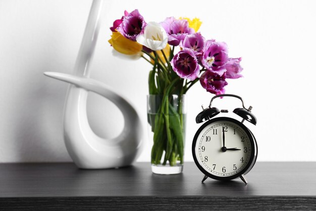 Alarm clock with tulips bouquet on table